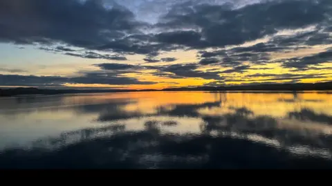 Dark blue clouds and orange sky at sunset reflected in a loch