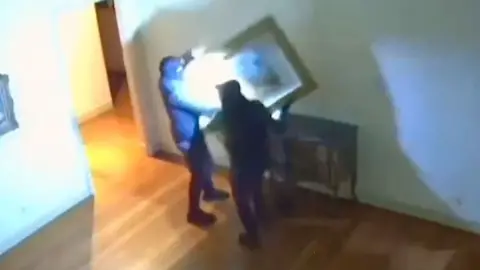 A still from CCTV footage shows two thieves taking artwork off a wall inside a museum in Italy.