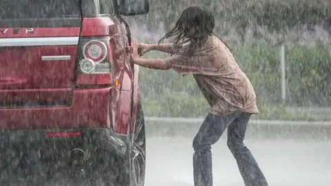 A girl gets into a car during driving rain
