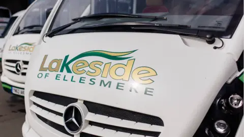 A zoomed in photo of a white mini bus with Lakeside of Ellesmere printed on the front and a Mercedes badge.