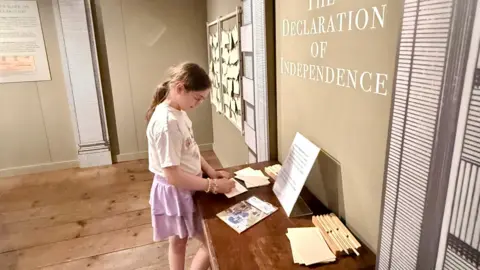 Peter Hall A girl writes on a piece of paper next to a display that reads "Declaration of Independence"