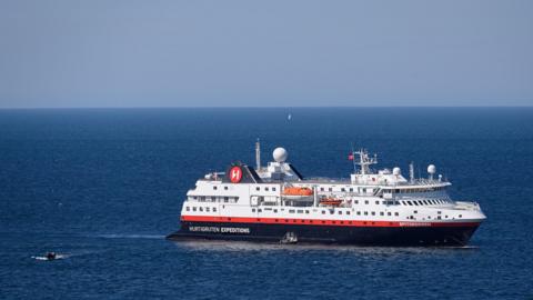 A close-up of a small cruise ship on a sunny day with a tender headed towards it