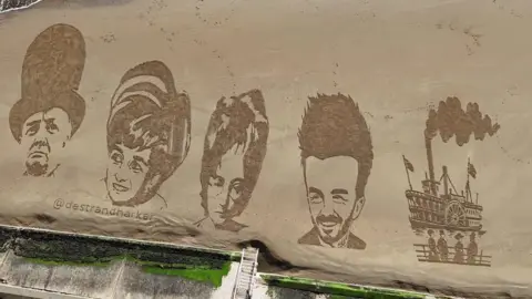 A birds-eye view of a sandy beach with drawings of Winston Churchill, Princess Diana, John Lennon, David Beckham and an old-fashioned ship, all etched onto the surface.