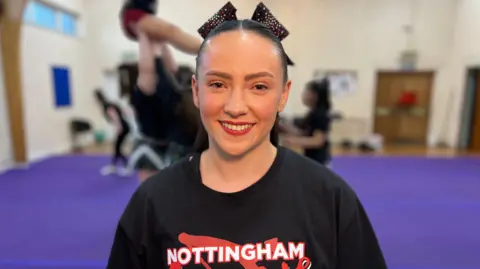 Georgie Leckey, looking at the camera, dressed in loose t-shirt with her Cheerleading group logo on it