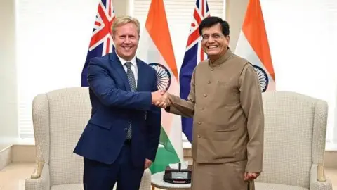 India's federal Commerce and Industry Minister Piyush Goyal (right, in grey Indian traditional attire) and New Zealand's Minister for Trade and Investment Todd McClay (in blue suit) pictured as both countries launched a free trade deal with flags of the two countries in the background.