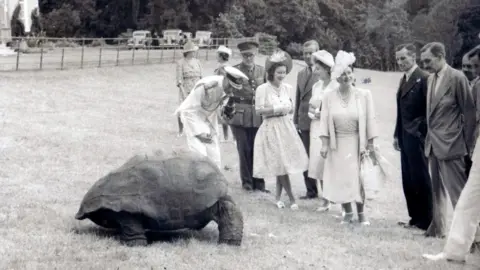 PA Media A black-and-white image of Jonathan surrounded by a group of people in formal attire, including Queen Elizabeth II