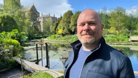 A man stands in front of a lake.
