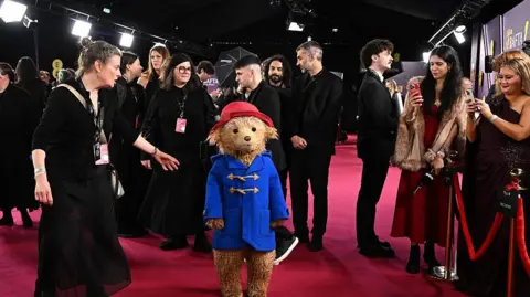 Getty Images for BAFTA Paddington on the red carpet being photographed by the press and ushered forward by a person 