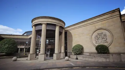 PA Media a sandstone court building with columns at the entrance and a large crest off to one side.
