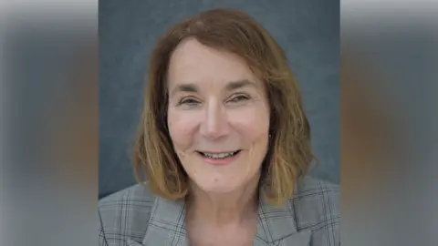 Babergh District Council A portrait photo of Deborah Saw. She has shoulder length light brown hair and wears a chequered grey blazer. She is smiling at the camera. 