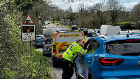 Dorset Police Cars and vans left on verges along both sides of a rural road - a police officer is talking to one driver