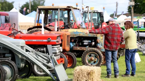 The image shows a man and woman looking at a line of red tractors.
