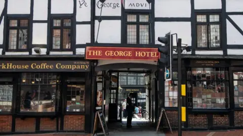 The entrance to The George Hotel is displayed via a red sign hanging above an entrance way off a street.