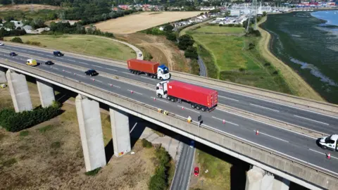 Traffic crossing over the Orwell Bridge in Suffolk, cones in place, and people working on the bridge