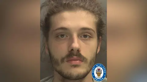 West Midlands Police A police custody photograph of a young man with light brown hair tied back and short facial hair. He is looking directly at the camera with a neutral expression against a plain grey background. The West Midlands Police logo is visible in the bottom right corner of the image.