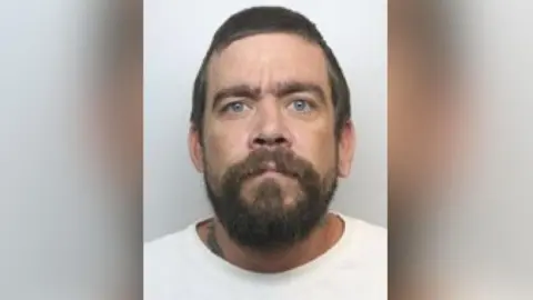 South Yorkshire Police A police photograph of Harrison, who has blue eyes and dark brown hair. He sports a full beard and appears to have a tattoo on his lower neck area.