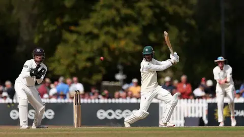 Rehaan Edavalath plays an attacking shot on the off side at Cheltenham College, watched by Gloucestershire wicketkeeper James Bracey. 
