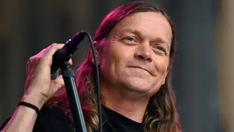 Brad Arnold standing on stage next to a microphone stand
