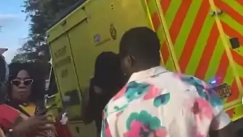 A large yellow emergency vehicle is in the background with people standing in front.