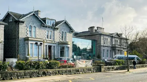 The Albyn School building in Aberdeen, with vehicles parked outside and one one person walking along the street.