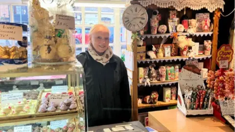 AMELIA RILEY/BBC Carol Barden stood behind the till inside the shop that is filled with sweets and cakes 