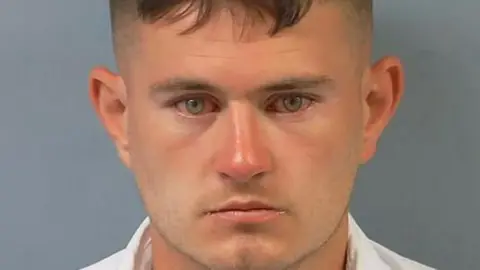 Hampshire and Isle of Wight Constabulary A police "mugshot" photo of Stephen Rennie. He is clean shaven, has dark hair and green eyes. He is wearing a white shirt.