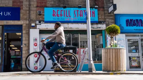 A man cycles past a Refill Station vape shop on Greenock's high street. The sign is bright blue and red.