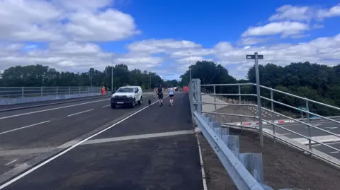 Close up of the bridge with white van travelling over it and people walking along the side.