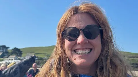 A woman with brunette wavy hair and sunglasses smiling
