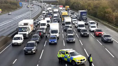 PA Media Police closing the M25, where a demonstrator, from Just Stop Oil, has climbed the gantry.