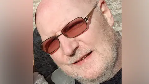 PA Media Man's face wearing sunglasses and smiling with grey stubble