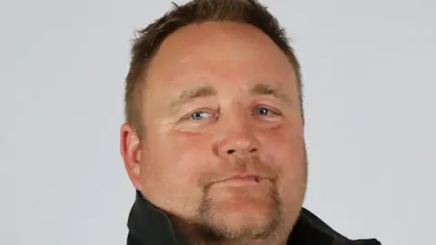Jason Hutchings, Torbay councillor, in a black top with the collar up