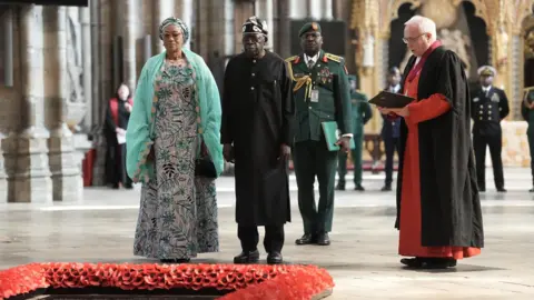 PA Media President of Nigeria Bola Ahmed Tinubu and First Lady Oluremi Tinubu stand in front of the Grave of the Unknown Warrior, a memorial stone framed with red poppies, during a visit to Westminster Abbey.