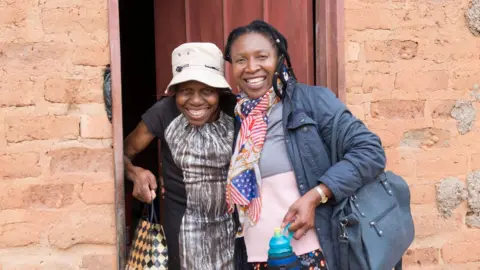 Glenn Edwards A photo of Martha and a friend standing outside a home in Zimbabwe