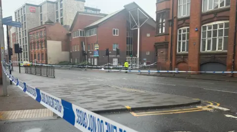 Police tape over a main road in the centre of Leicester with an officer stationed inside the cordon