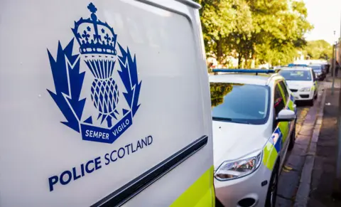 Police Scotland van and cars parked on a tree-lined street