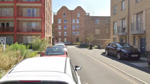 A street view of Eagle Street in Cambridge. It is a residential street with parked vehicles, bushes and trees on either side of the road.