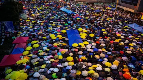 Getty Images Umbrellas are opened as tens of thousands come to the main protest site one month after the Hong Kong police used tear gas to disperse protesters October 28, 2014 in Hong Kong