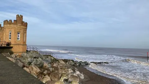 The sea at Withernsea stretching out into the distance. Rocks on the shore and a small tower are on the left.