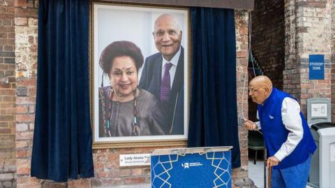 Framed portrait Lady Aruna Swraj Paul and Lord Swraj Paul hanging on a wall behind curtains opened by Lord Paul to officially rename the building