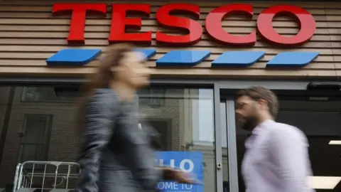 Getty Images Two people walk past a Tesco store