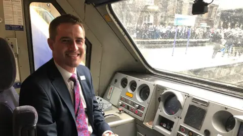 c2c Man with short dark hair and wearing a suit sitting in the driver's seat of a train