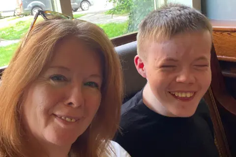 Louise Johnstone Louise and her son Leo are sitting next to each other. They are both smiling. Leo has short hair and is wearing a black t-shirt and Louise has a pair of glasses resting on her head.