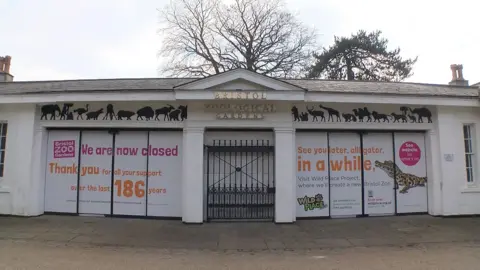 The front doors of Bristol Zoo in Clifton after the site was closed. It has words saying we are closed and see you later alligator with a closed gate.
