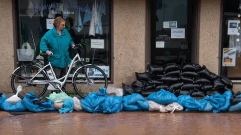 Getty Images A woman looks at sandbags piled up in front of a shop and to protect against flood water in Erftstadt, Lechenich, western Germany, on July 16, 2021.