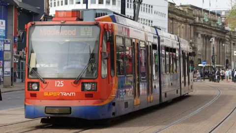 A tram running in Sheffield city centre. The supertram is painted blue and red and the front sign reads "Middlewood".