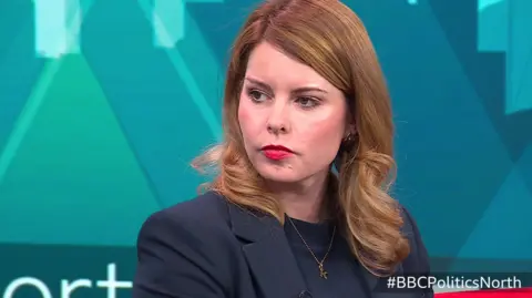 Kim McGuinness sits with the teal set of BBC Politics North behind here, she's wearing a navy blue suit and looking sternly to the left hand side.