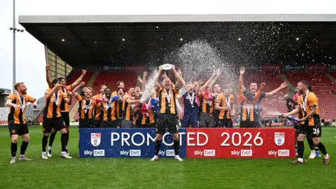 PA Media Michael Morrison holding a silver shield with other team-mates standing behind him celebrating. 