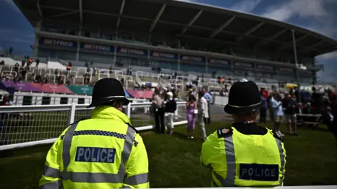 Police officers monitor crowds in front of the grandstand at the Epsom Derby.