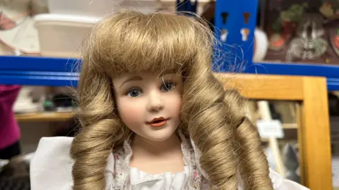 A China doll with long curled blonde hair stares at the camera